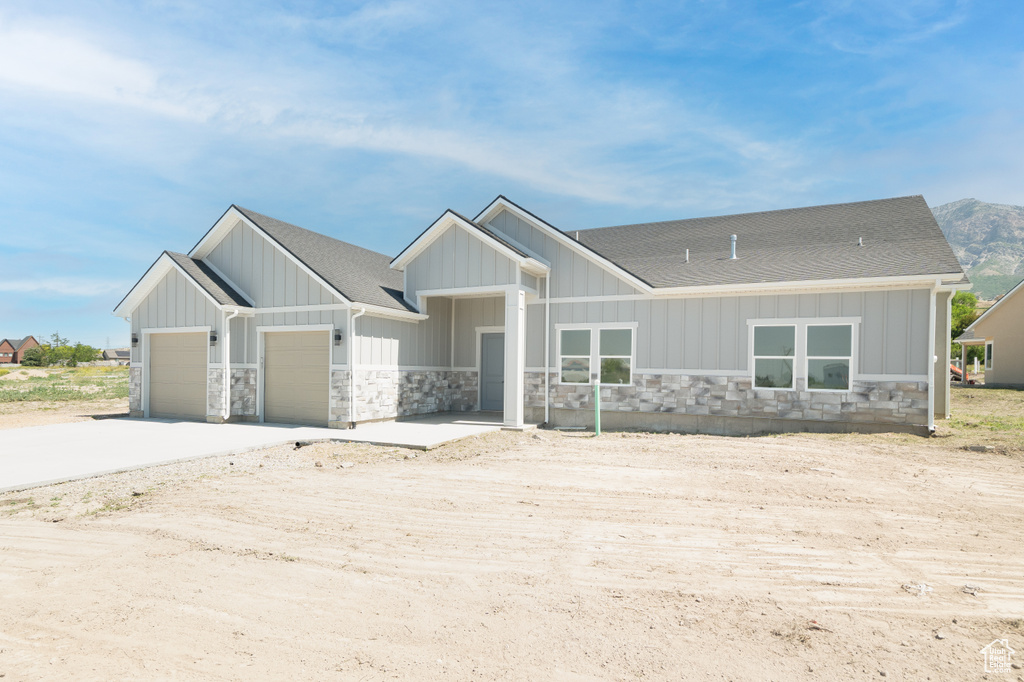 View of front of house featuring stone siding, a shingled roof, an attached garage, concrete driveway, and board and batten siding