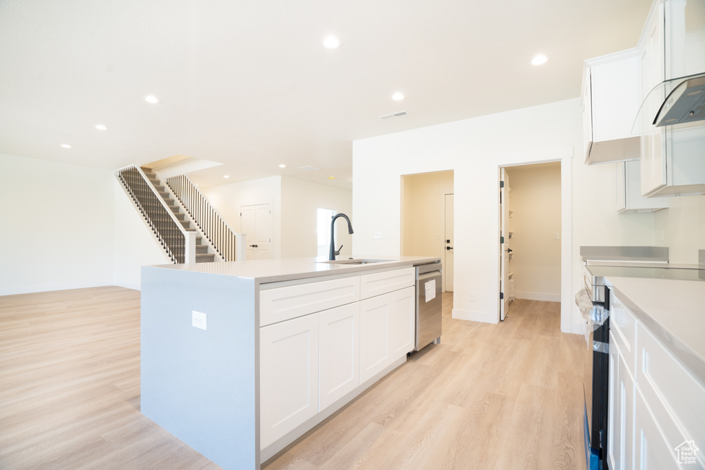 Kitchen featuring appliances with stainless steel finishes, a kitchen island with sink, light wood-type flooring, white cabinets, and recessed lighting