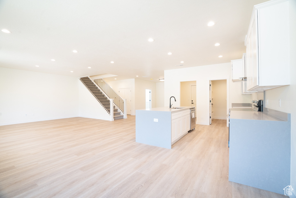 Kitchen with appliances with stainless steel finishes, a kitchen island with sink, white cabinets, light wood-type flooring, and recessed lighting