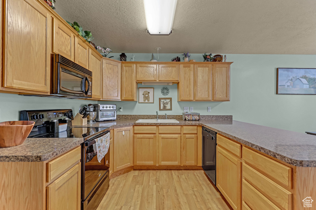 Kitchen featuring black appliances, a peninsula, light wood-type flooring, light brown cabinetry, and a textured ceiling