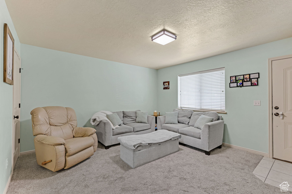 Living room featuring a textured ceiling, light colored carpet, and light tile patterned flooring