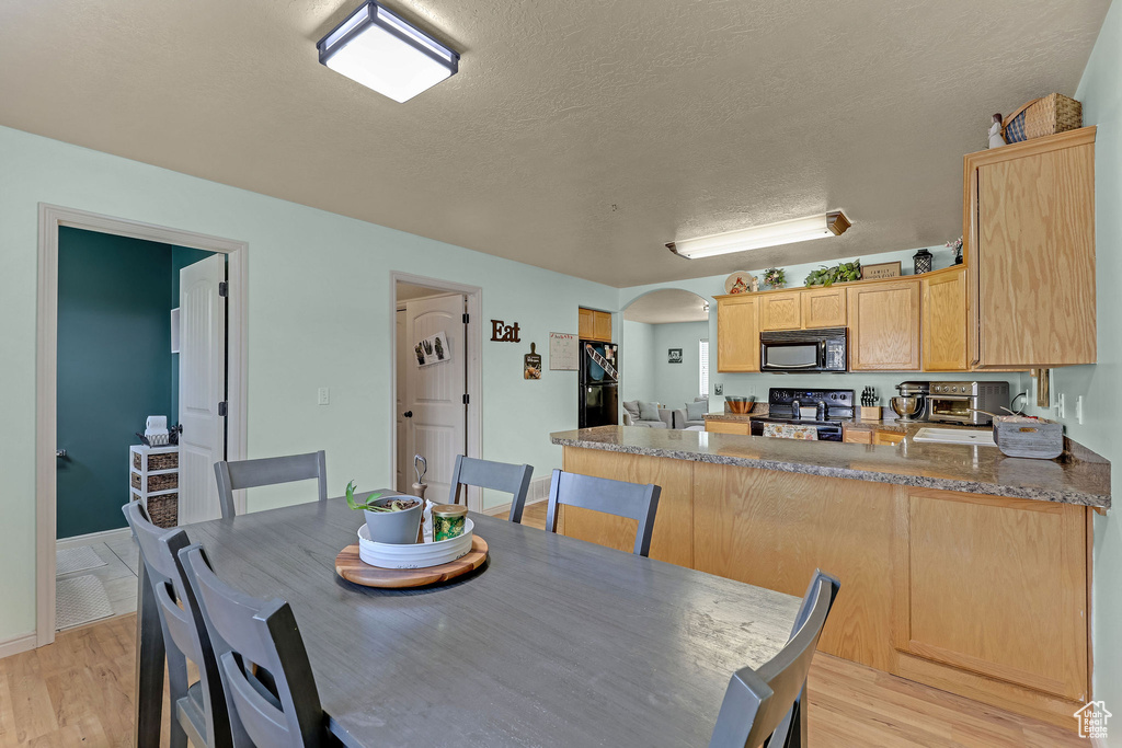 Dining room featuring arched walkways, light wood-style floors, and a textured ceiling