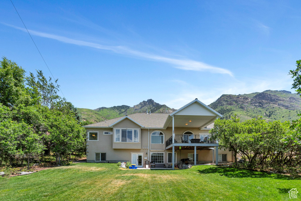 Rear view of property with stucco siding, a mountain view, a lawn, a patio, and a balcony
