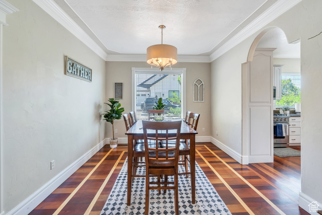 Dining area with dark wood-type flooring, arched walkways, and ornamental molding