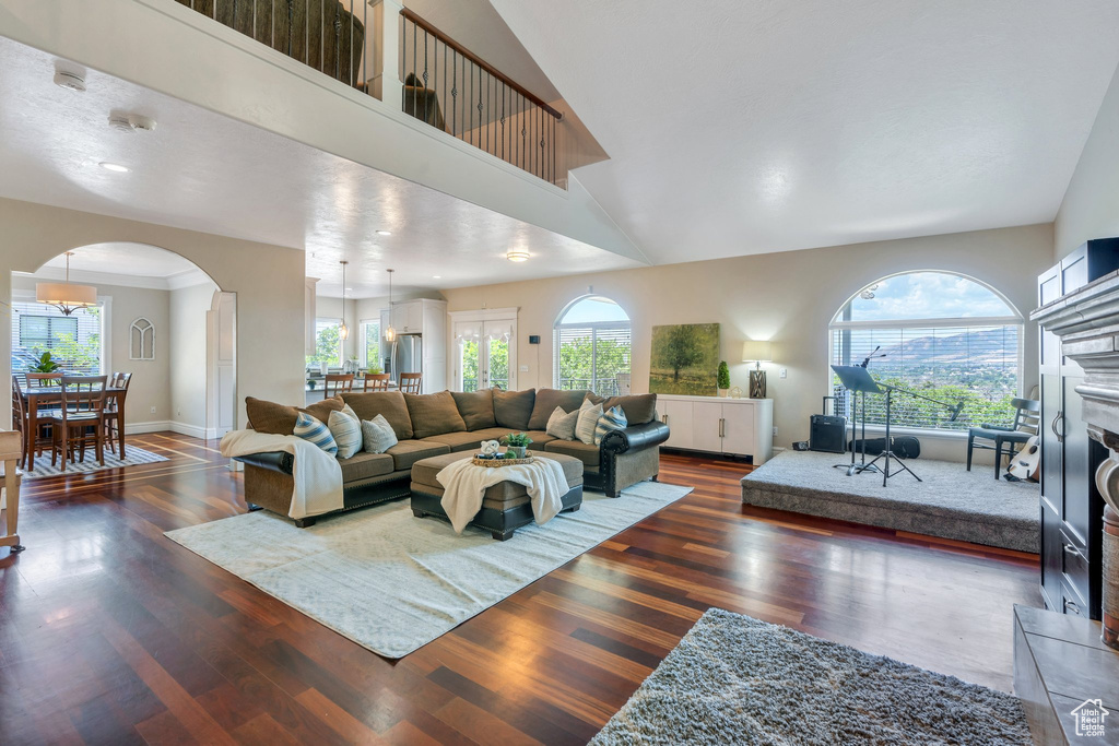 Living room featuring arched walkways, plenty of natural light, dark wood-style floors, and a towering ceiling