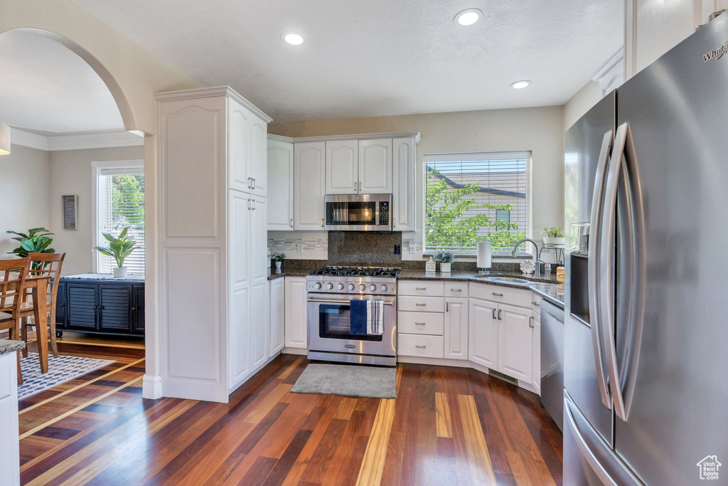Kitchen with stainless steel appliances, dark wood-style floors, white cabinetry, arched walkways, and recessed lighting
