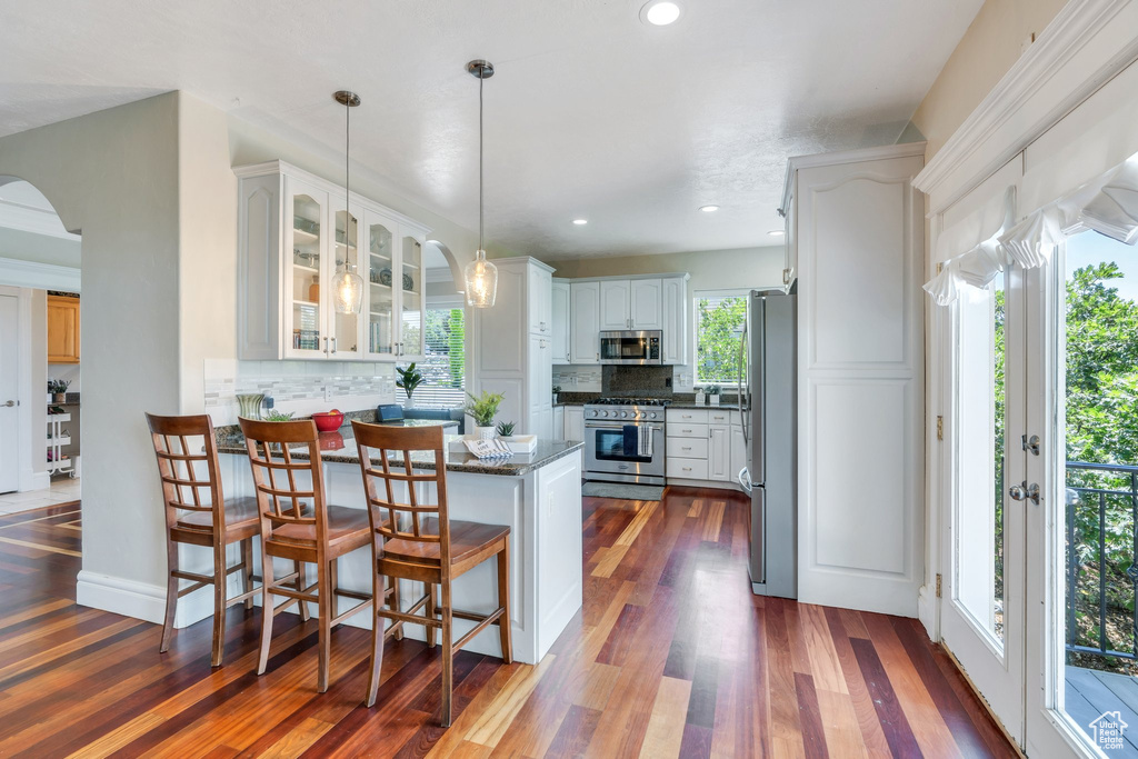 Kitchen with appliances with stainless steel finishes, a peninsula, glass insert cabinets, decorative backsplash, and arched walkways