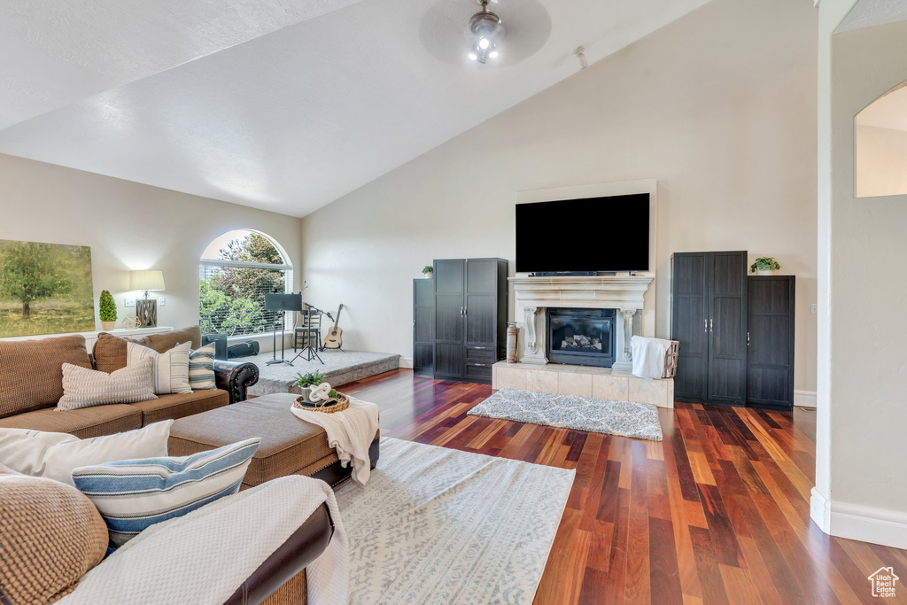 Living room featuring a ceiling fan, high vaulted ceiling, dark wood-style floors, a tiled fireplace, and arched walkways