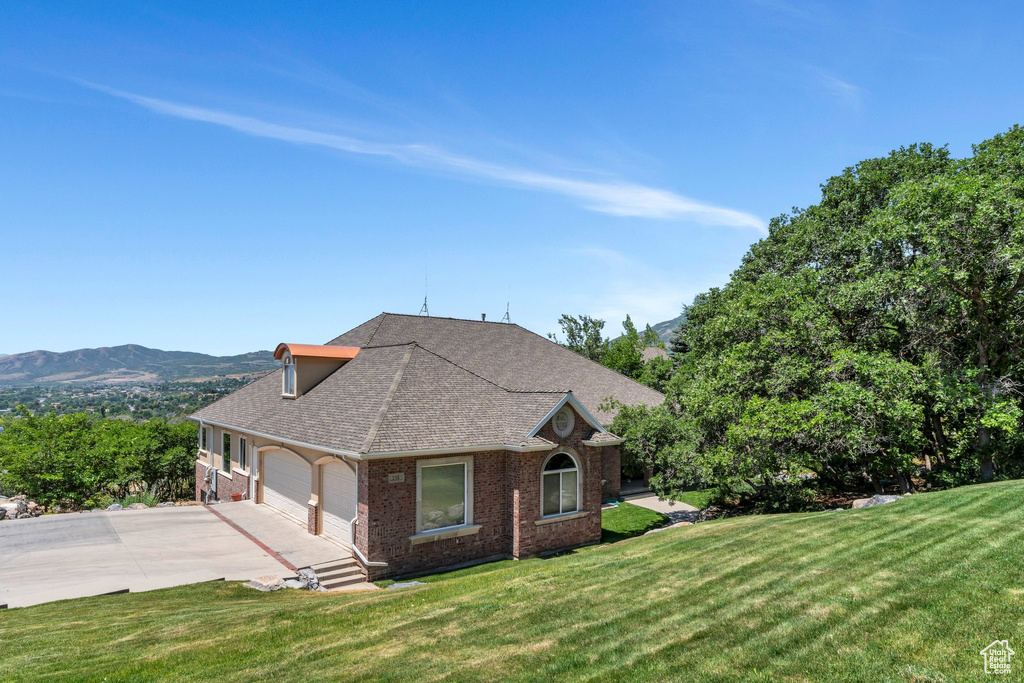 View of property exterior with brick siding, concrete driveway, an attached garage, a shingled roof, and a lawn