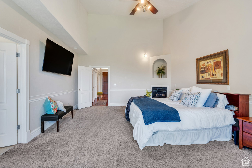 Carpeted bedroom with high vaulted ceiling, ceiling fan, and a glass covered fireplace