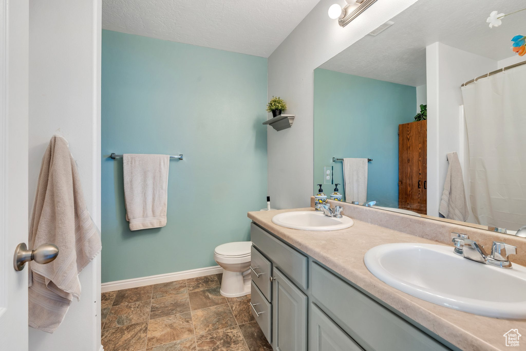 Bathroom featuring double vanity, stone finish flooring, and a textured ceiling