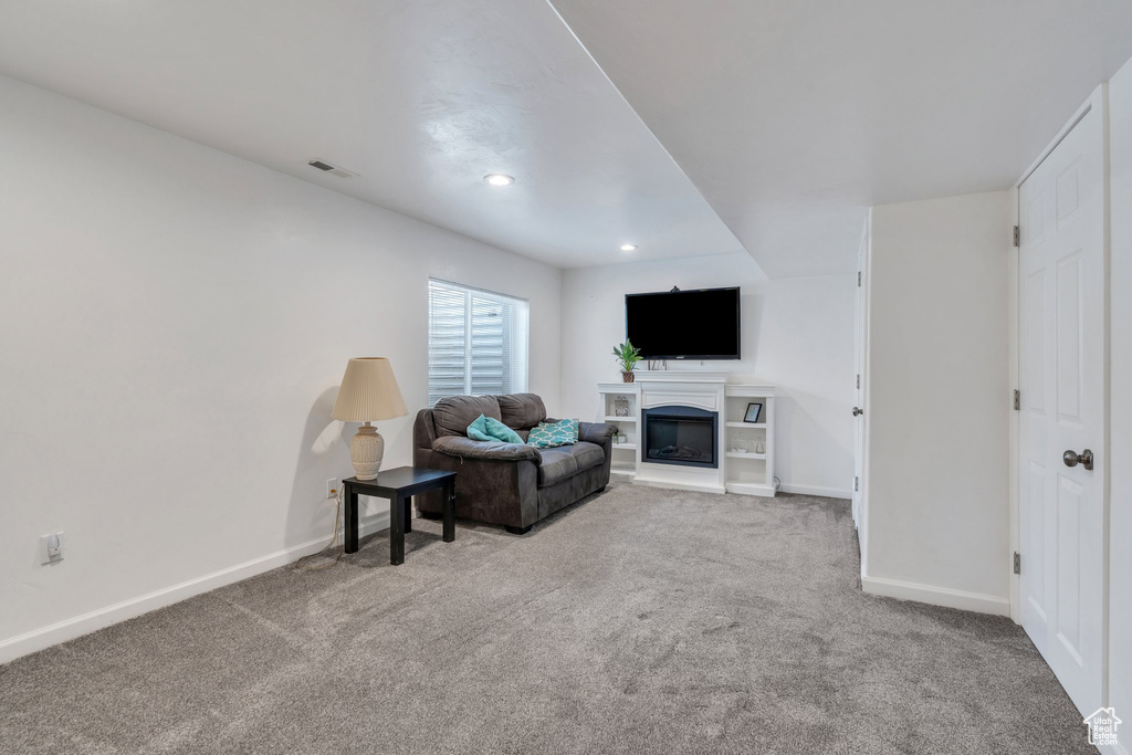 Living area with carpet flooring, a glass covered fireplace, and recessed lighting