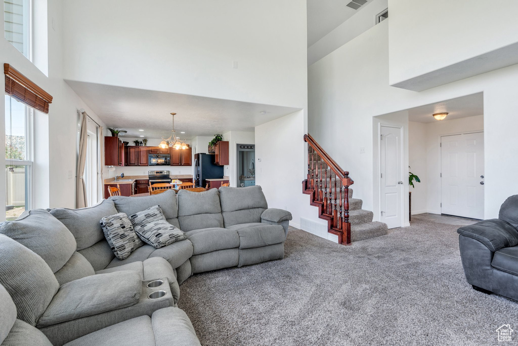 Carpeted living area with a high ceiling, a chandelier, and stairs