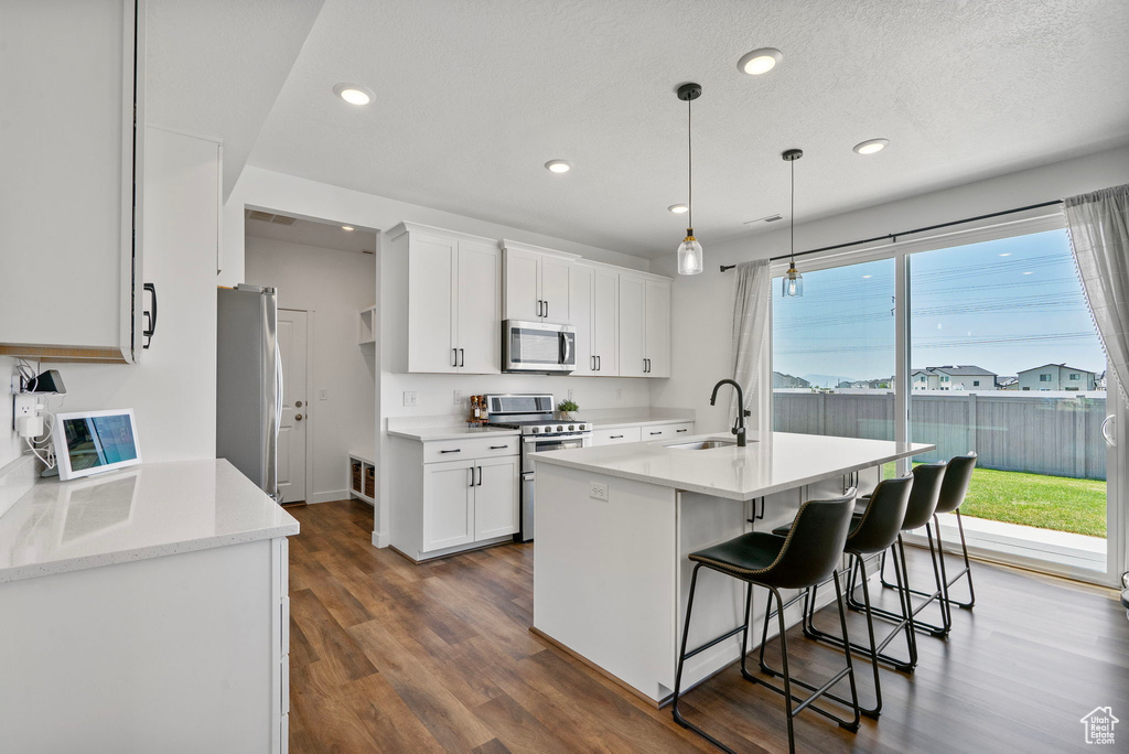 Kitchen with appliances with stainless steel finishes, white cabinets, dark wood-type flooring, recessed lighting, and a breakfast bar