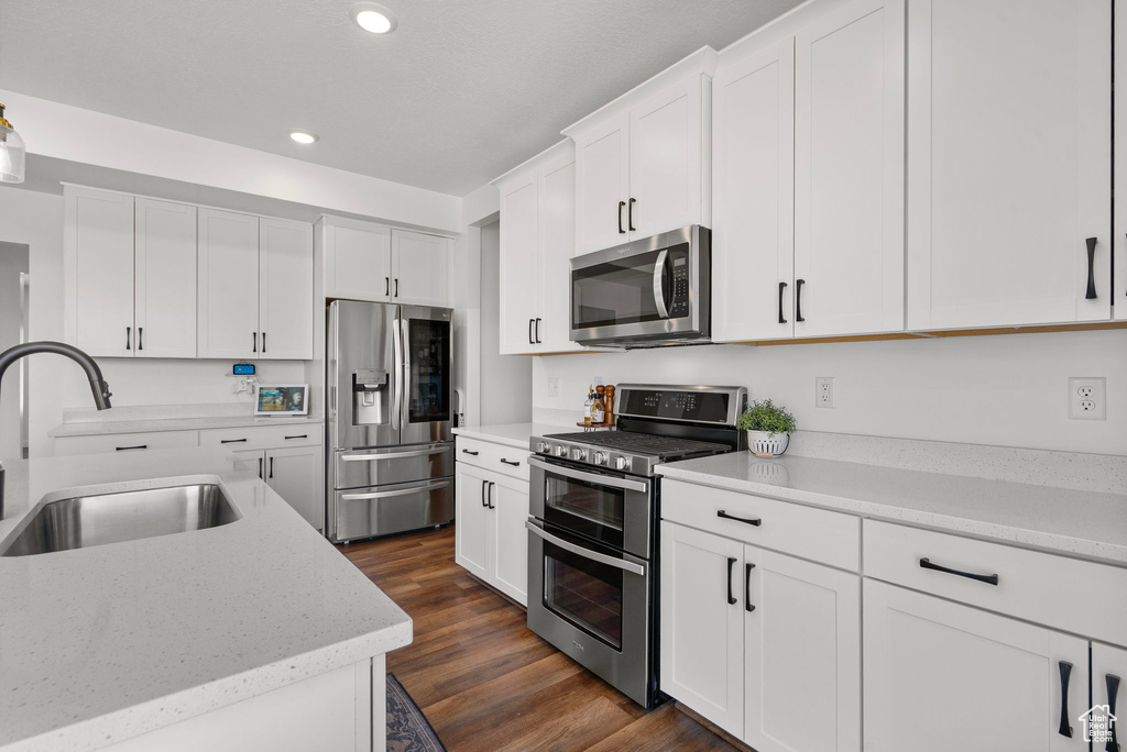 Kitchen with appliances with stainless steel finishes, recessed lighting, white cabinets, dark wood-type flooring, and light stone counters