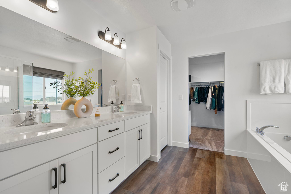 Full bathroom with double vanity, a garden tub, wood finished floors, and a spacious closet
