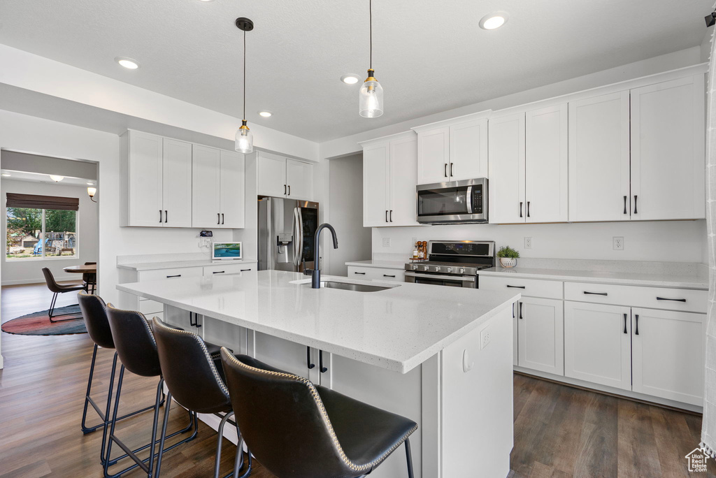 Kitchen featuring stainless steel appliances, an island with sink, light countertops, recessed lighting, and white cabinets
