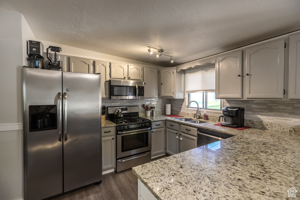 Kitchen with appliances with stainless steel finishes, tasteful backsplash, dark wood-style floors, a textured ceiling, and light stone countertops