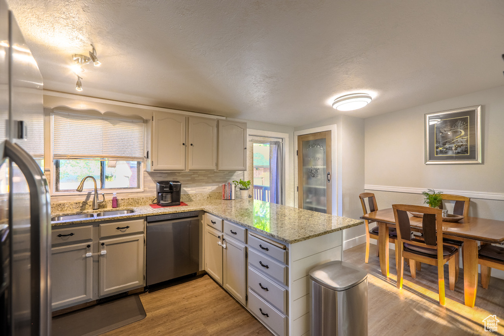 Kitchen with appliances with stainless steel finishes, a peninsula, light wood finished floors, a textured ceiling, and light stone countertops