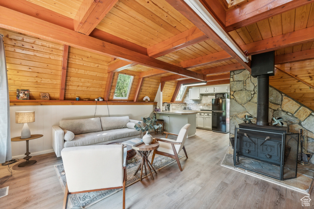 Living room featuring a wood ceiling with exposed beams, light wood-style floors, wooden walls, and a wood stove