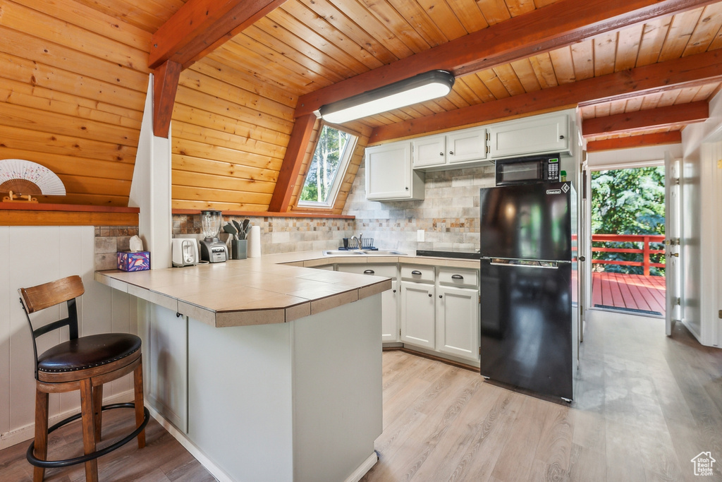 Kitchen with black appliances, a peninsula, a wooden ceiling with exposed beams, plenty of natural light, and white cabinetry