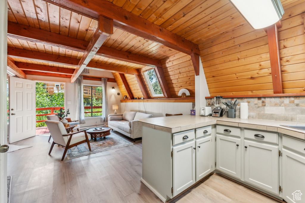 Kitchen featuring a wood ceiling with exposed beams, a peninsula, light wood-style floors, tile counters, and open floor plan