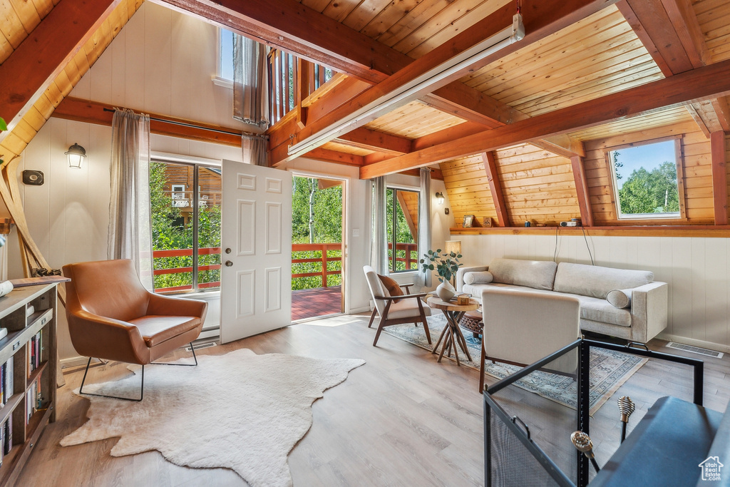 Living area featuring healthy amount of natural light, a wood ceiling with exposed beams, wood finished floors, and wooden walls