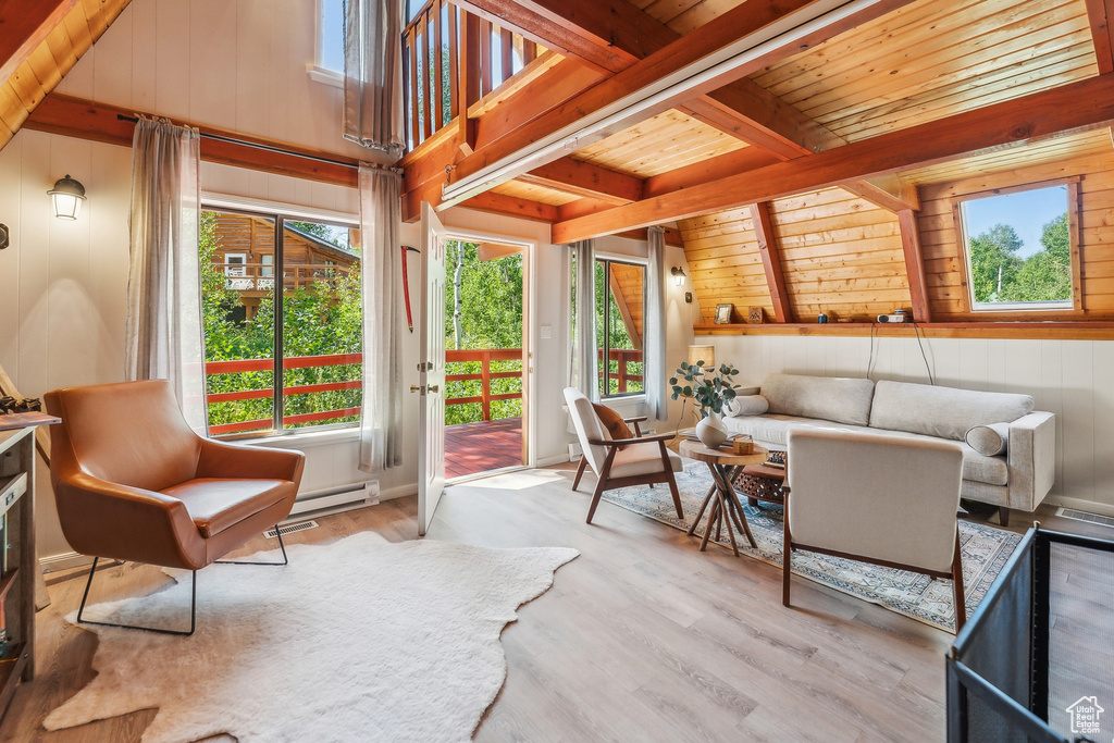 Living area with a wood ceiling with exposed beams, healthy amount of natural light, wood walls, wood finished floors, and baseboard heating