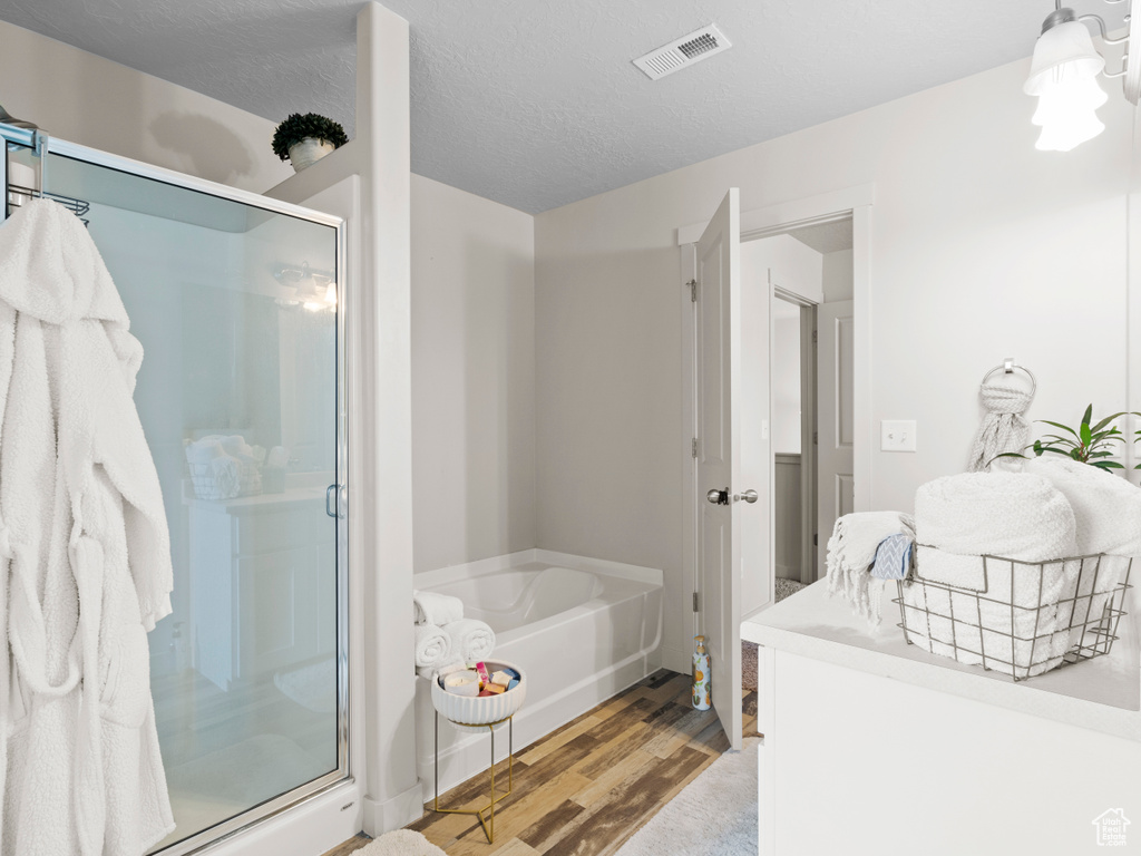 Bathroom with a stall shower, wood finished floors, a bath, a chandelier, and a textured ceiling