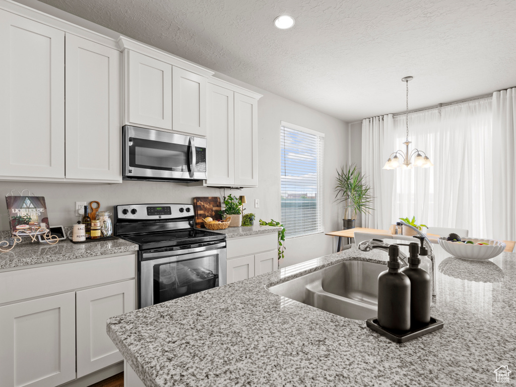 Kitchen featuring appliances with stainless steel finishes, white cabinets, a chandelier, a textured ceiling, and decorative light fixtures