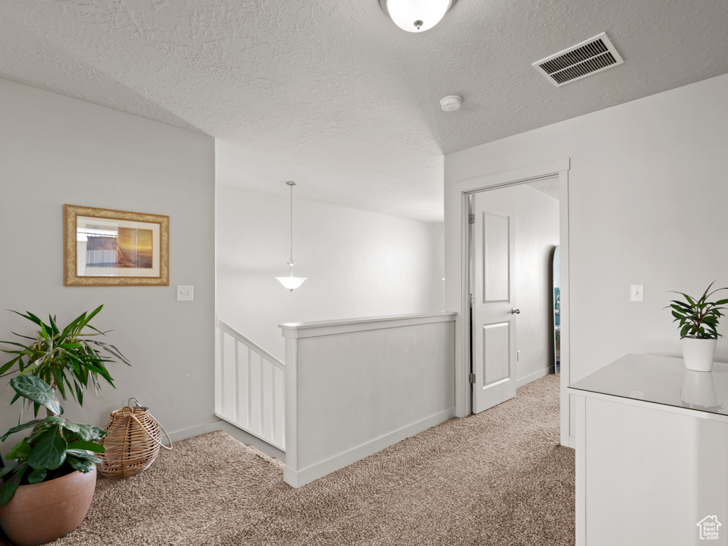 Hall with an upstairs landing, light carpet, and a textured ceiling