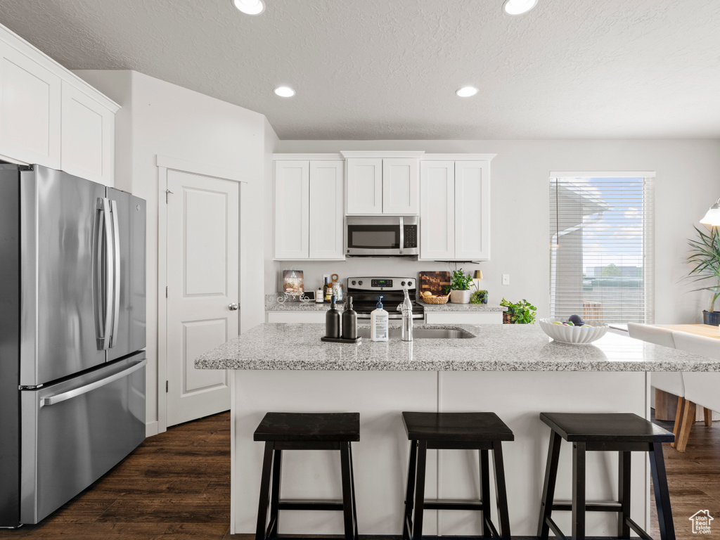 Kitchen with appliances with stainless steel finishes, white cabinets, a kitchen breakfast bar, light stone counters, and recessed lighting