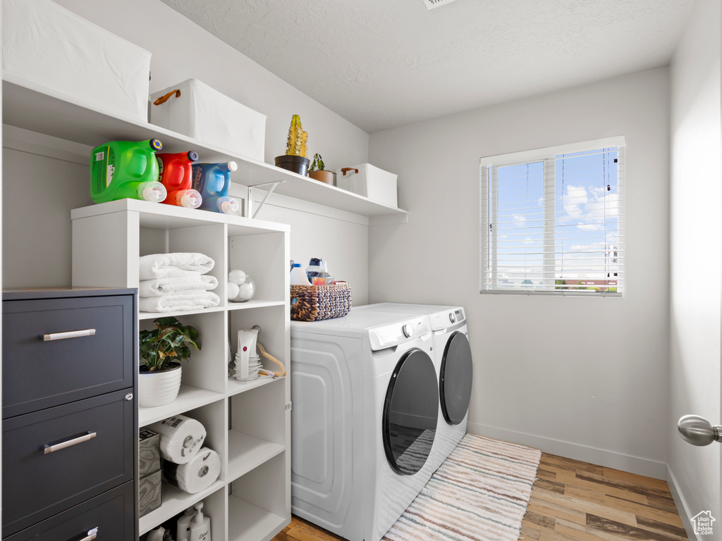Washroom with washing machine and dryer, light wood-type flooring, and a textured ceiling