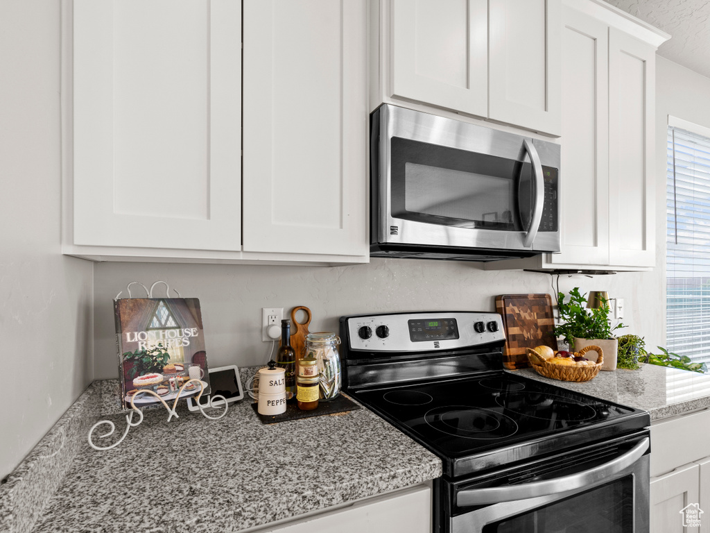 Kitchen featuring stainless steel appliances, white cabinetry, and light stone countertops