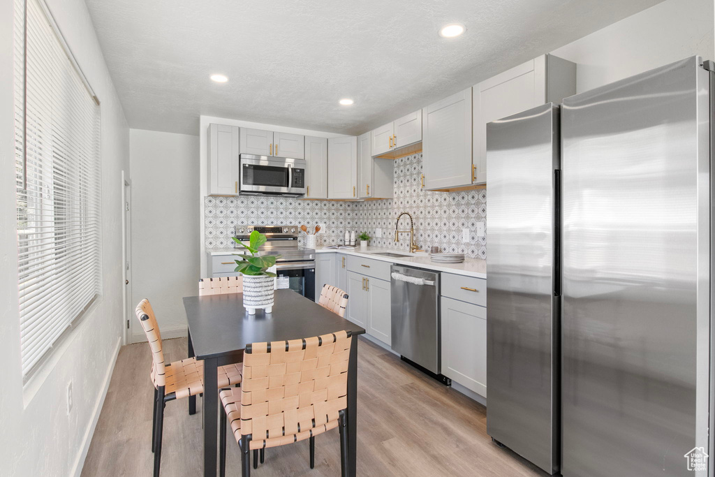 Kitchen with stainless steel appliances, decorative backsplash, gray cabinetry, light wood finished floors, and recessed lighting