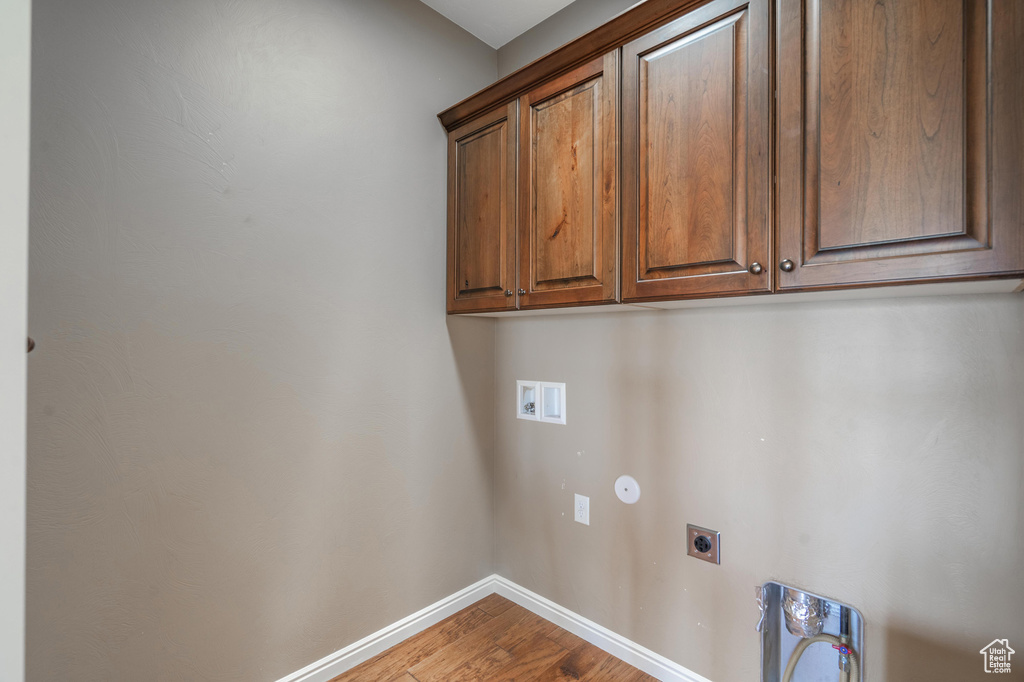 Washroom with hookup for an electric dryer, cabinet space, wood finished floors, and washer hookup