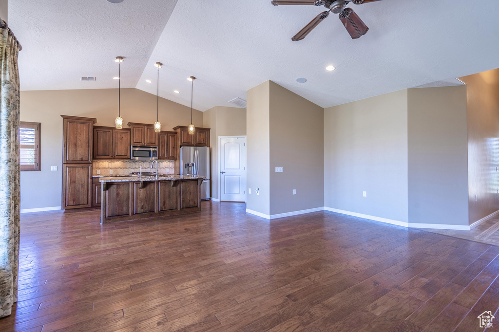 Kitchen featuring stainless steel appliances, a ceiling fan, a kitchen breakfast bar, a center island with sink, and dark wood-style flooring