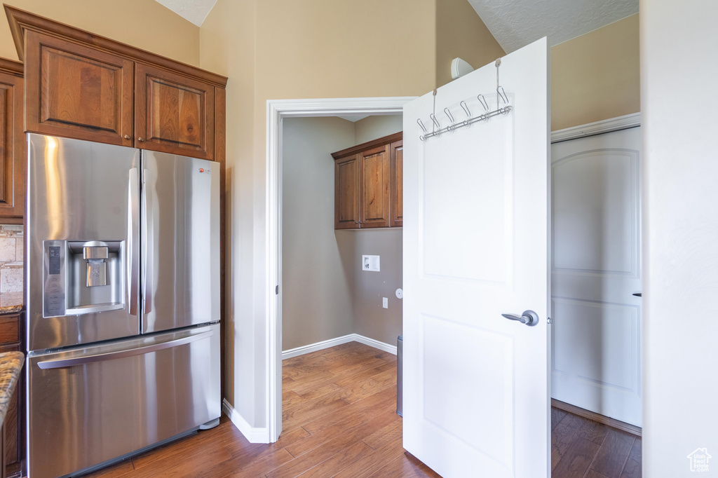Kitchen with stainless steel fridge, light wood finished floors, brown cabinetry, and stone counters