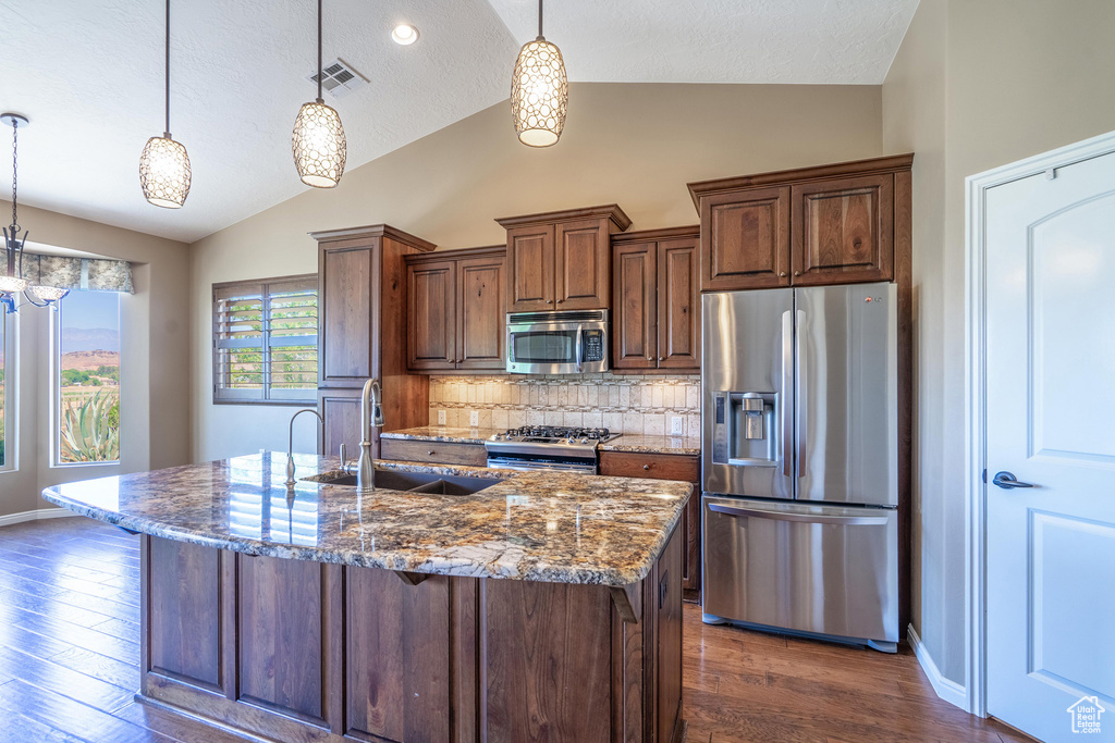 Kitchen featuring appliances with stainless steel finishes, vaulted ceiling, dark stone counters, tasteful backsplash, and dark wood-type flooring