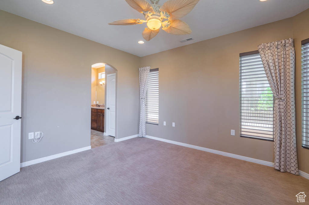 Unfurnished bedroom with arched walkways, light colored carpet, multiple windows, recessed lighting, and ensuite bath