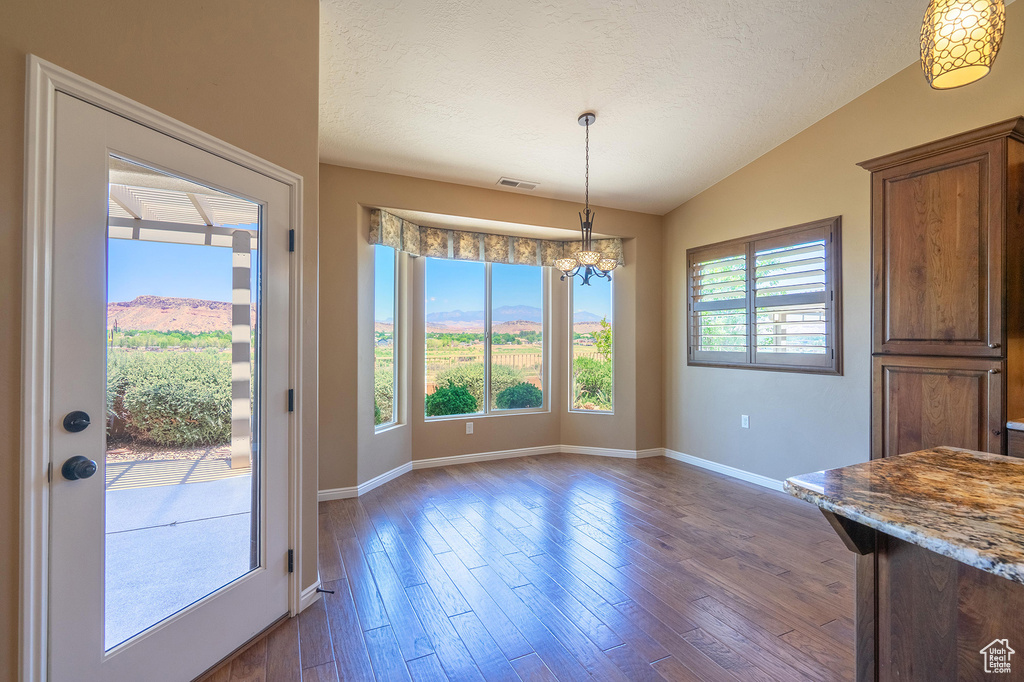 Unfurnished dining area featuring vaulted ceiling, a chandelier, dark wood-style flooring, and a textured ceiling