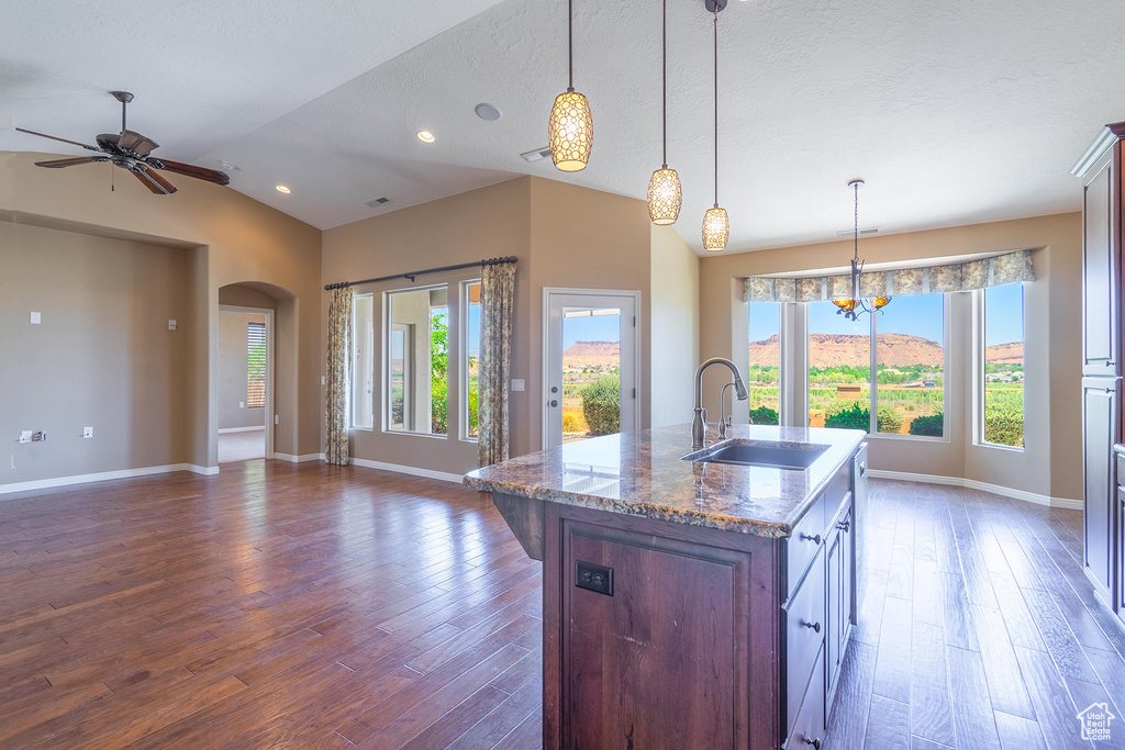 Kitchen featuring dark wood-style floors, arched walkways, a ceiling fan, a center island with sink, and lofted ceiling