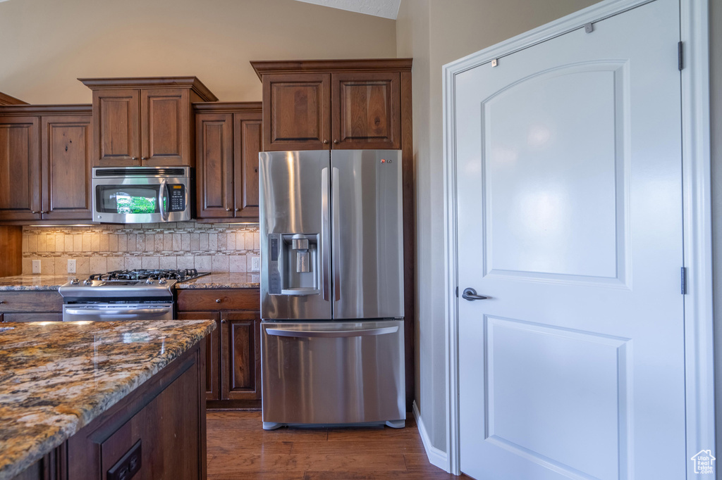 Kitchen featuring stainless steel appliances, backsplash, dark wood finished floors, stone counters, and lofted ceiling