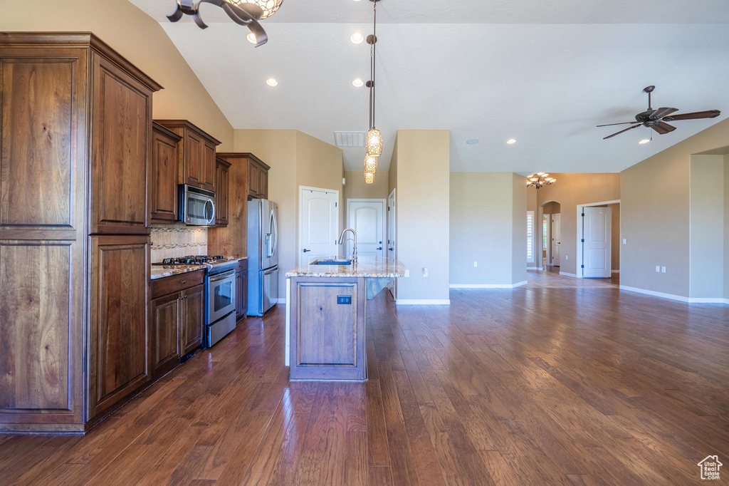 Kitchen with appliances with stainless steel finishes, open floor plan, arched walkways, decorative backsplash, and a center island with sink