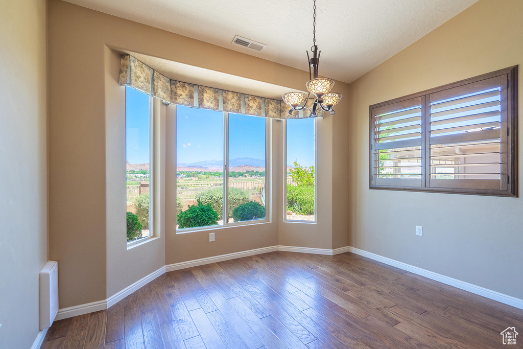 Spare room with plenty of natural light, a chandelier, and wood-type flooring