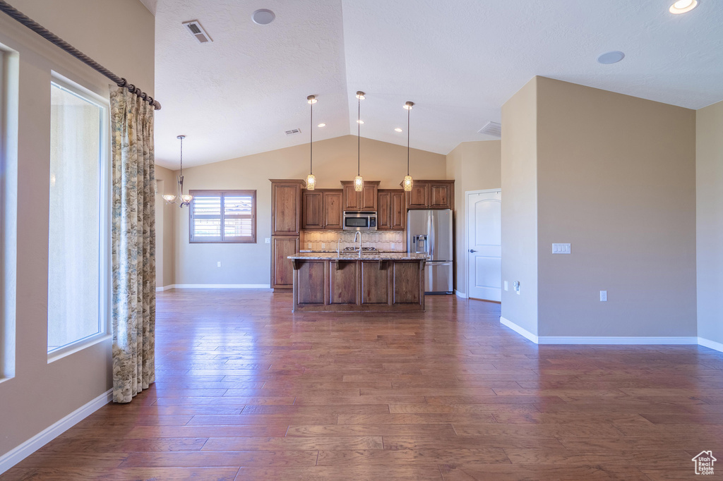 Kitchen with appliances with stainless steel finishes, vaulted ceiling, dark wood-style flooring, open floor plan, and a breakfast bar