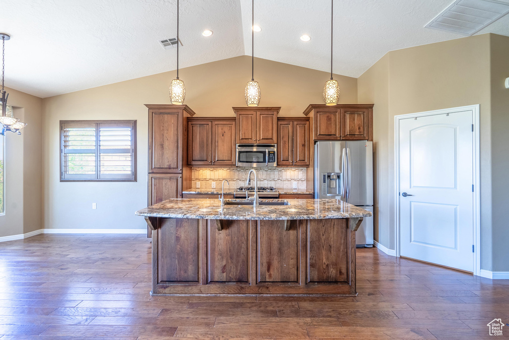 Kitchen featuring appliances with stainless steel finishes, stone counters, lofted ceiling, a breakfast bar, and dark wood-style flooring
