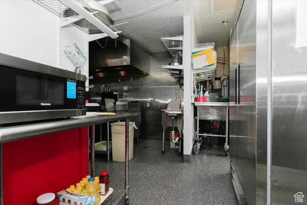 Kitchen with stainless steel appliances, wall chimney range hood, and speckled floor