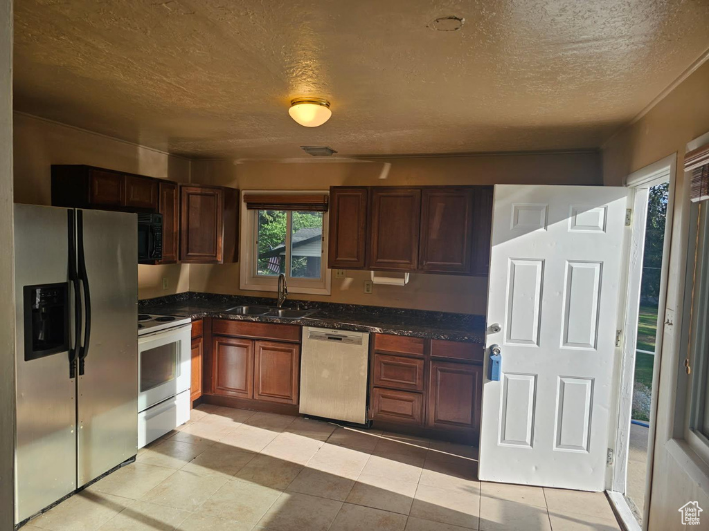 Kitchen featuring appliances with stainless steel finishes, a textured ceiling, light tile patterned floors, and dark stone counters