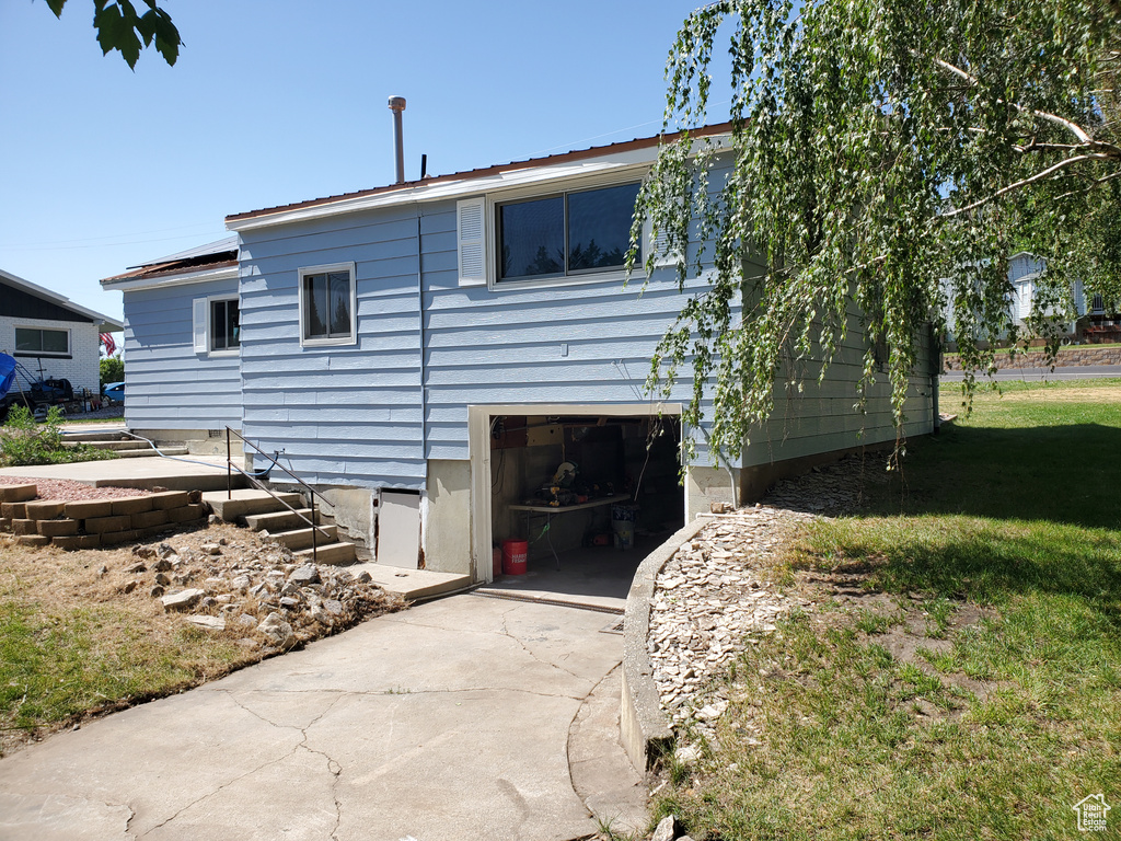 Rear view of property featuring a garage, concrete driveway, a lawn, and solar panels